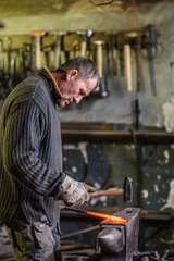 A blacksmith forging a red-hot iron billet on an anvil with a hammer. Handicraft concept