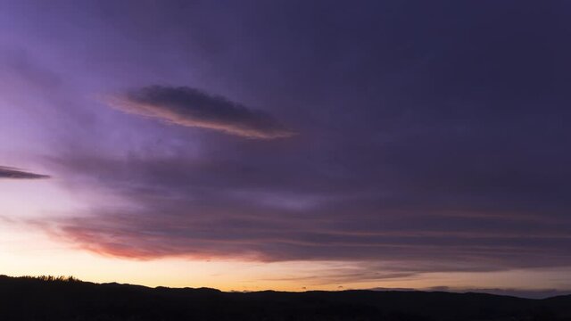 Dark purple and blue clouds glow with sunset light in sky, Timelapse