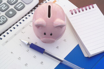 Saving money concept. Piggy bank on calendar with calculator, notepad and pen.