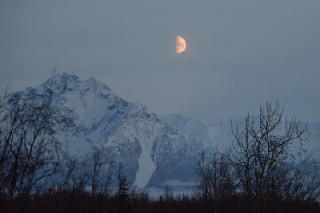 The moon rises behind Alaska's Chugach Range at sunset.