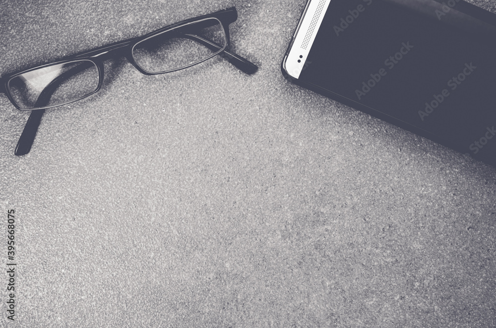 Poster grayscale shot of smartphone and eyeglasses on a rough stone background with copy space