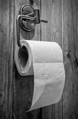 A roll of toilet paper in a holder on a black and white photo.