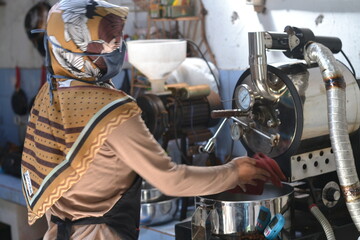 A female coffee roaster is roasting coffee beans using a roasting machine