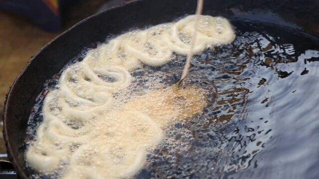 Frying Jalebi. Hands pouring Jalebi batter in oil in circular shapes.