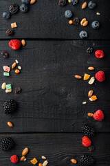 Frame made of mixed dried and raw ripe berry and fruits with nuts, top view with copy space, on black wooden table