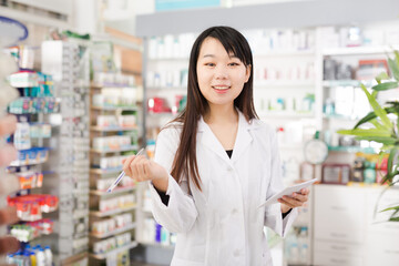 Chinese woman pharmacist keeps track of drugs in interior of pharmacy. High quality photo