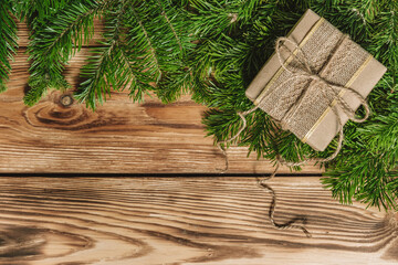 Christmas card with a gift in craft packaging and fir branches on a wooden background. Top view. Space for text.