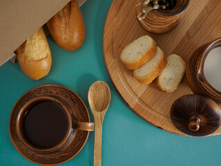 Flat lay of breakfast made from cup of black tea, French baguette and milk on green background top view. To create an atmosphere of warmth, comfort, at home, the photo is supplemented with a wooden