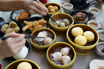 Close up hand picking up dim sum with chopsticks and enjoying a variety of Chinese dim sum in the...