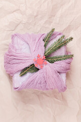 gift wrapped in pink textile with fir branches on beige background.
