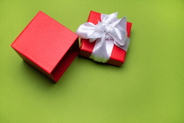 Open red gift box with white ribbon on green background: Christmas background or happy birthday