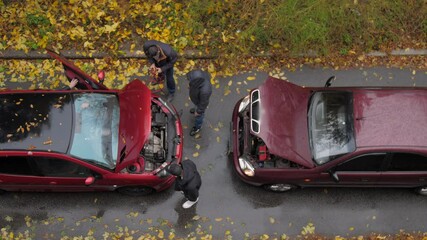 People hold coloured cables standing between red cars with opened hoods on grey road with yellow leaves slow motion. Concept road accident