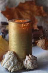 Tall golden candle with dried flowers at the base and autumn background
