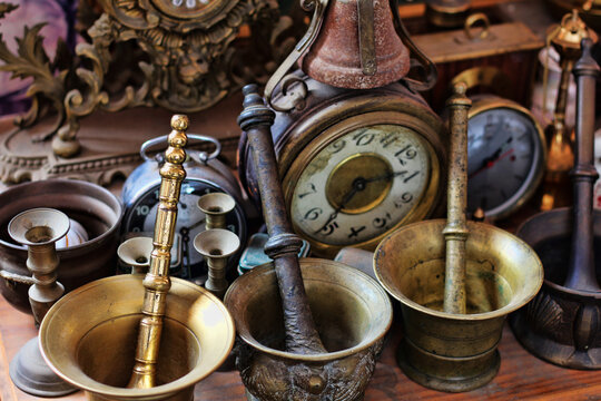 Closeup of antique metallic mortars, candle holders, alarm clocks, and a table clock