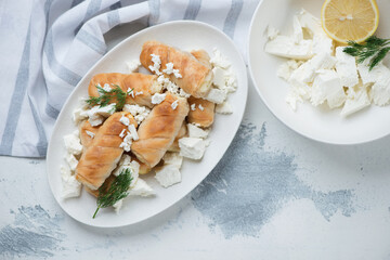 White plate with baked greek feta rolls, flatlay over white concrete background, horizontal shot with copyspace