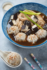 Asian soup with dumplings, udon noodles and tofu cheese served in a blue plate, vertical shot, selective focus