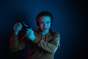 The gamer angry woman with headphones and joystick playing video games on dark blue background. Neon colored.