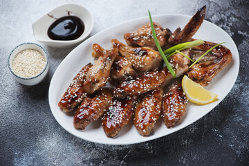 White oval plate with chicken wings baked in teriyaki sauce, horizontal shot on a dark grey stone background, elevated view