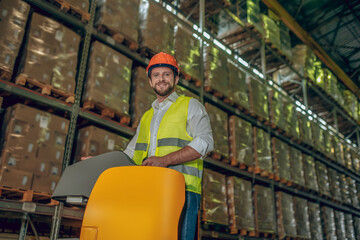 Fototapeta na wymiar Warehouse worker in orange helmet standing near shelves with containers