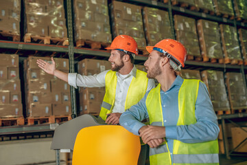 Warehouse worker in orange helmet showing something to his colleague