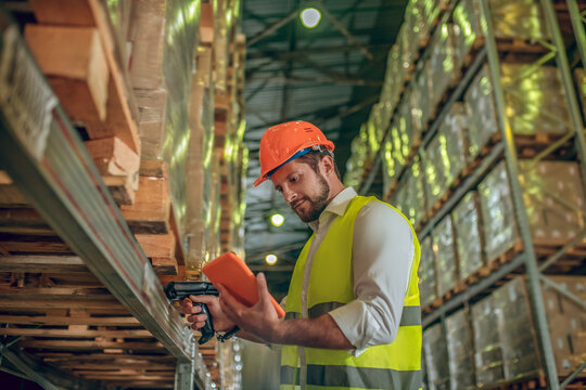 Warehouse Worker In Yellow Vest Looking At The Tablet