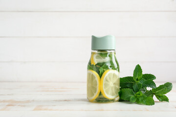 Bottle of water with fresh lemon and mint on light background