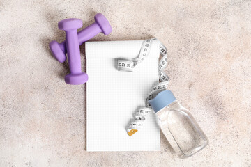 Bottle of clean water with notebook, dumbbells and measuring tape on light background