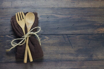 Wooden set spoon and fork with brown napkin on rustic wooden background. Top view, copy space for text.