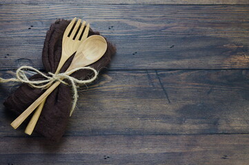 Wooden set spoon and fork with brown napkin on rustic wooden background. Top view, copy space for text.