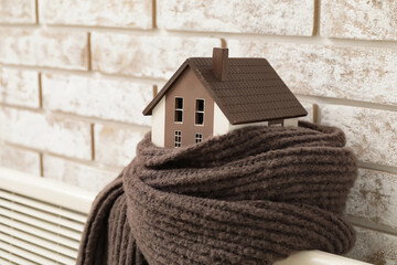 Figure of house and scarf on radiator. Concept of heating season