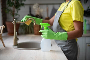 General cleaning of the kitchen. A woman in an apron and rubber gloves washes the sink....