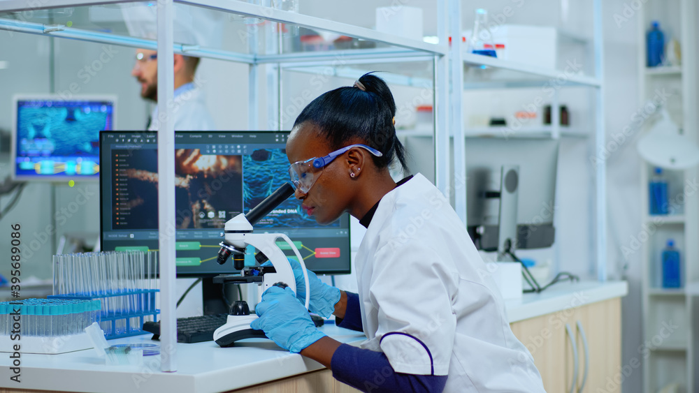 Aufkleber african scientist checking sample of virus using microscope in modern lab. multiethnic team examinin
