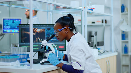 African scientist checking sample of virus using microscope in modern lab. Multiethnic team examining vaccine evolution using high tech for scientific research of treatment development against covid19 - obrazy, fototapety, plakaty