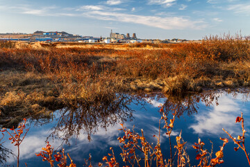 Naklejka na ściany i meble View of the tundra and industrial zone in the vicinity of an arctic settlement. Early summer in the Arctic. Reflection of the sky in the water. Neighborhood of the city of Anadyr. Chukotka, Russia.