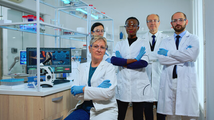 Multiethnic team of experienced scientists looking at camera in modern equipped lab. Group of doctors examining virus evolution with high tech and chemistry tools for scientific research, vaccine