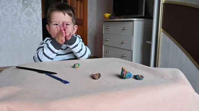 Toddler boy rolls plasticine in his little palms, moulds from plasticine on table, Child hands playing with colorful clay, day care close up, tactility activity.