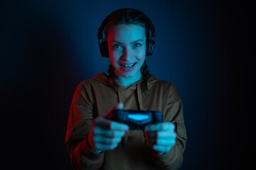 The gamer happy smiling woman with headphones and joystick playing video games on dark blue...