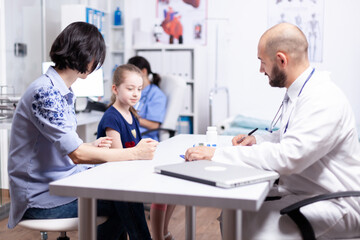 Pediatrician writing treatment after consultation of sick child in hospital office. Healthcare physician specialist in medicine providing health care services treatment examination.