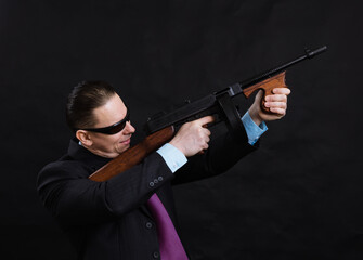 Mature gangster in sunglasses dressed in suit with tommy gun