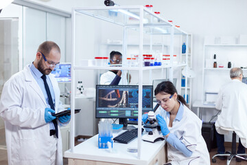 Chemist scientists doing vacine study in busy lab using tablet pc and miscroscope. Team of...