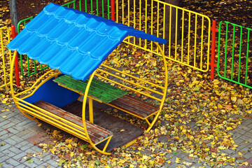 gazebo on the playground covered with yellow autumn leaves