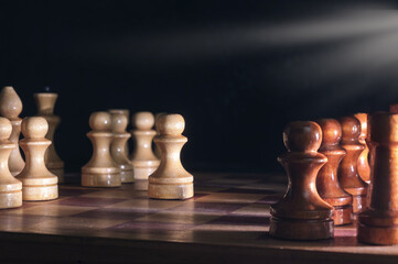 Wooden chess pieces and a chessboard on blurred dark background, selective focus