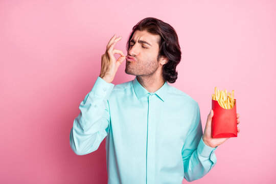 Photo portrait of man holding french fries in hand giving chef's kiss isolated on pastel pink colored background