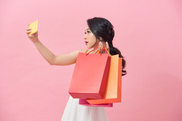 Fototapeta premium Happy pretty young woman with shopping bags makes photo self-portrait on the smartphone over colorful wall