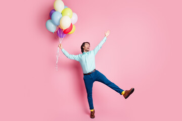Fototapeta na wymiar Photo portrait full body view of man spreading legs arms like star standing on one leg holding helium balloons isolated on pastel pink colored background