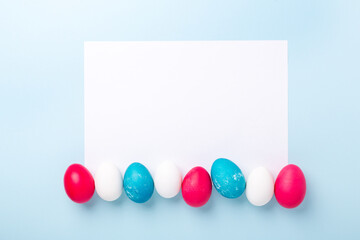 Easter composition with eggs and blank of white paper on blue background. Easter concept. Copy space. Top view