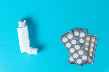 An open inhaler with medicine lies on a blue background with pills. Copy space. Flat lay. Top view