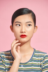 Fototapeta premium Young lovely asian woman with casual hairstyle touching her face with raised hand and looking aside flirty, isolated over pink background