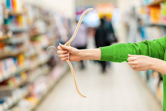 Female hands in a green sweater holding a clothes hanger in the form of a hunting bow. In the background, the trading floor. The concept of seasonal sales and shopping