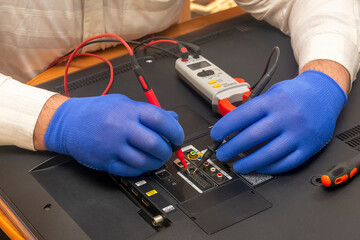 Engineer in service center repairs an LCD TV. Gloved hands measure the resistance on back of the monitor with multimeter. Selective focus, close-up.